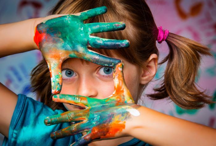 Girl looks through hands painted with paint