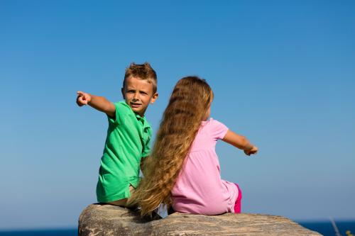 Boy and girl sitting on rock pointing in opposite directions