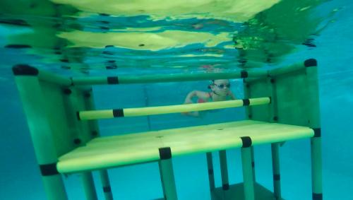 A QUADRO jungle gym under water with a girl swimming in the background